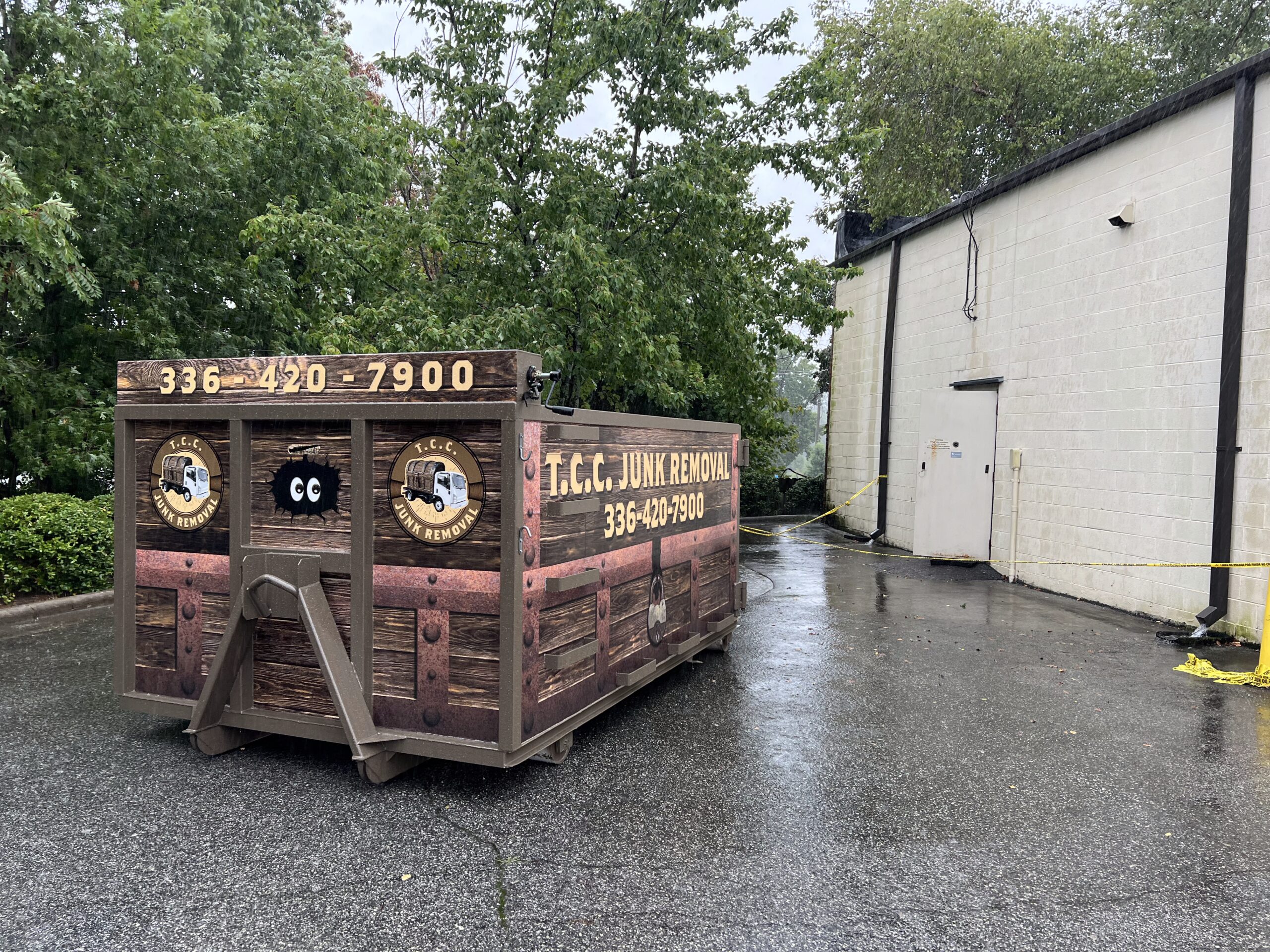 T.C.C. Junk Removal dumpster near building on rainy day.