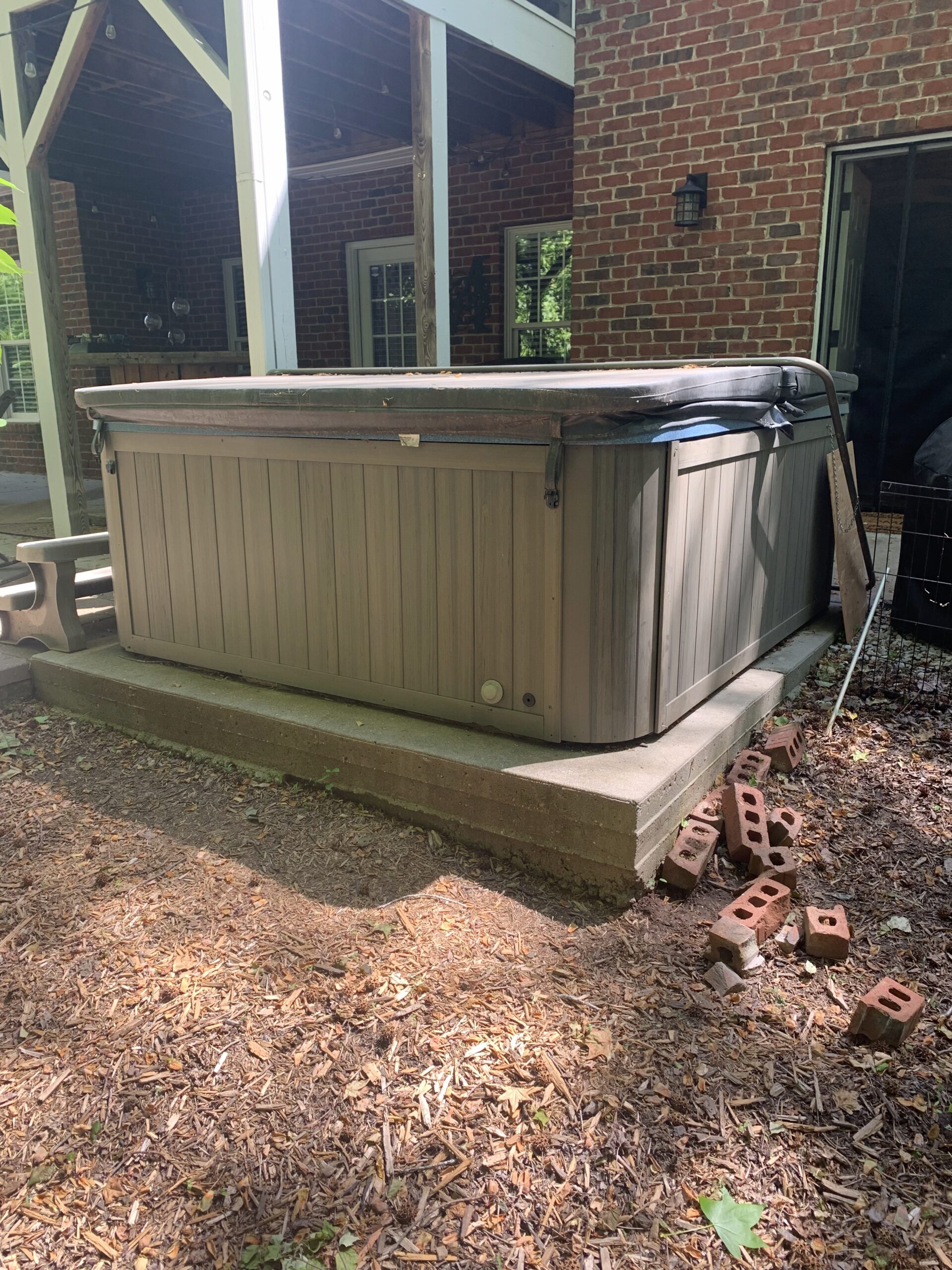 Outdoor hot tub on concrete slab with bricks nearby.