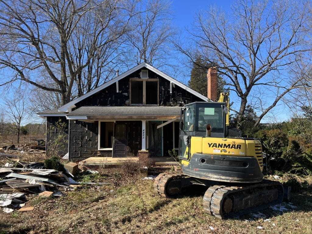 Excavator in front of house being demolished.