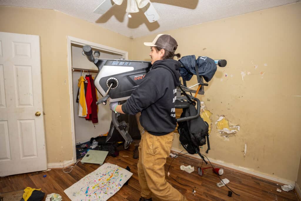 Man carrying exercise bike in messy room